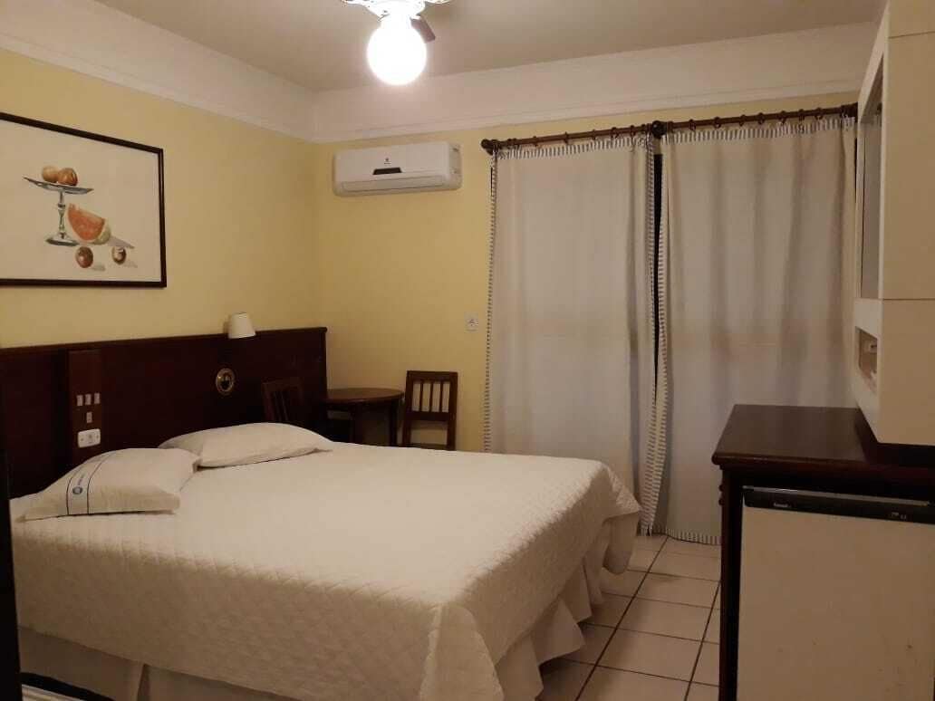 Une chambre d’hôtel équipée d’un lit, d’un bureau, d’une chaise, d’une fenêtre avec des rideaux et d’un climatiseur fixé au mur.