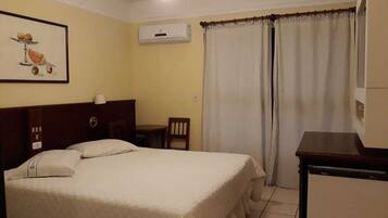 Une chambre d’hôtel équipée d’un lit, d’un bureau, d’une chaise, d’une fenêtre avec des rideaux et d’un climatiseur fixé au mur.