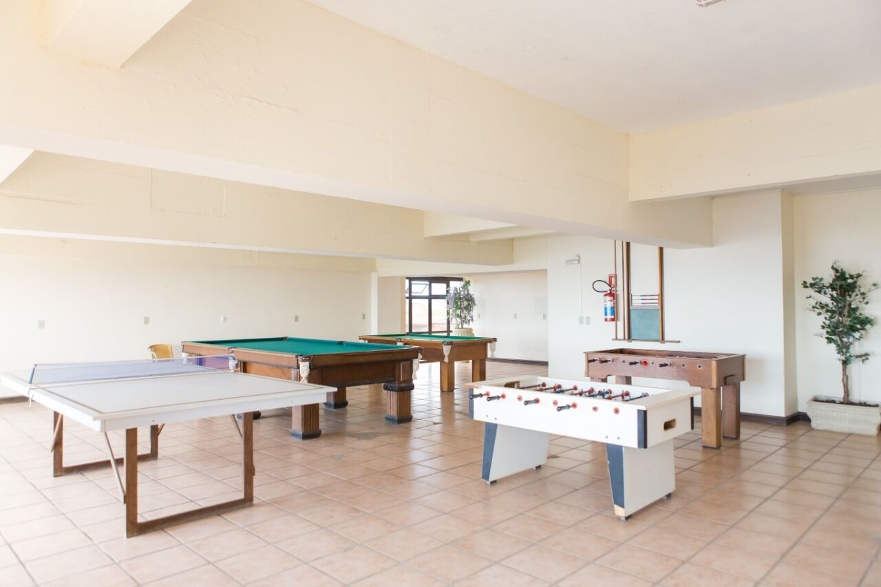 Un vaste espace de loisirs intérieur comprenant une table de baby-foot, une table de billard et une table de ping-pong.