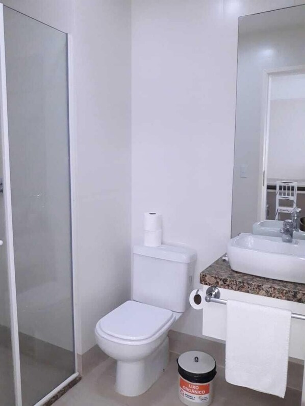 A bathroom with a toilet, sink, and glass shower door. - Hotel Araçá (Capao da Canoa)
