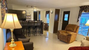 A living room with a TV, a dining area with chairs, a sofa, and a red chair.