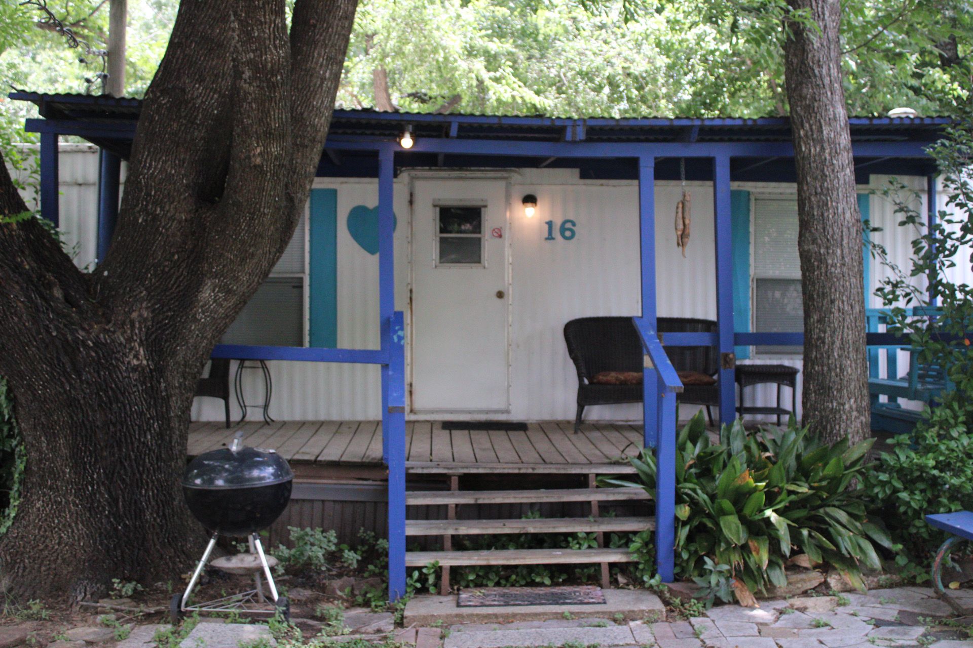 A covered porch with a grill, a chair, and a door marked with the number 16.