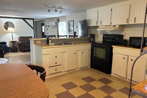 A compact kitchen with a stove, microwave, and coffee maker. There is a dining area with a table and chairs.