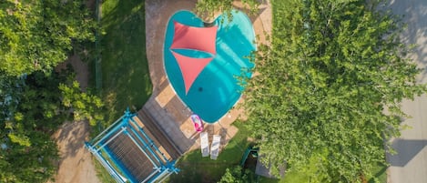 Vista aérea de una piscina con una sombra con forma de corazón, rodeada de follaje y una cerca azul.