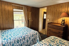 A room with two beds, a dresser, a lamp, and a door leading to another room.