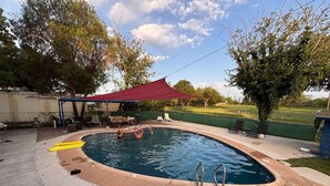 Piscina exterior con toldo rojo, rodeada de sillas de descanso y una zona de estar cubierta.
