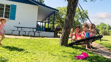 Children playing on a swing set in a grassy area with a picnic table and a building in the background.