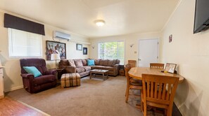 A living room with a sectional sofa, a coffee table, a dining table with chairs, a lamp, and artwork on the walls. - Weekly Stays Water View Suite with Covered Balcony (Kingsland)