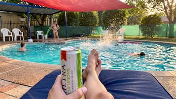 A person relaxing by a pool with a can of drink in hand.