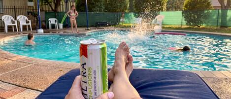 Une personne se détend au bord d’une piscine, une boisson à la main.