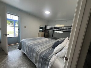 A bedroom with a bed, a dresser, a mirror, and a door leading to a patio. - Lakefront Suite - 15 (Kingsland)