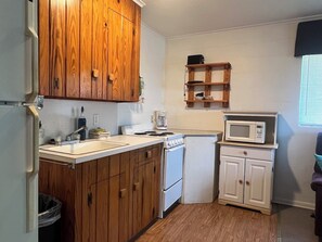 Una cocina compacta con armarios de madera, una encimera blanca, una estufa, un microondas y un estante pequeño.