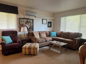 Una sala de estar con un sofá marrón, un sillón morado, una mesita y una lámpara.