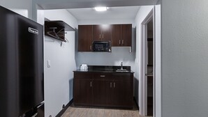 Une cuisine de taille réduite, avec des meubles de couleur bois foncé, un réfrigérateur noir et un four à micro-ondes.