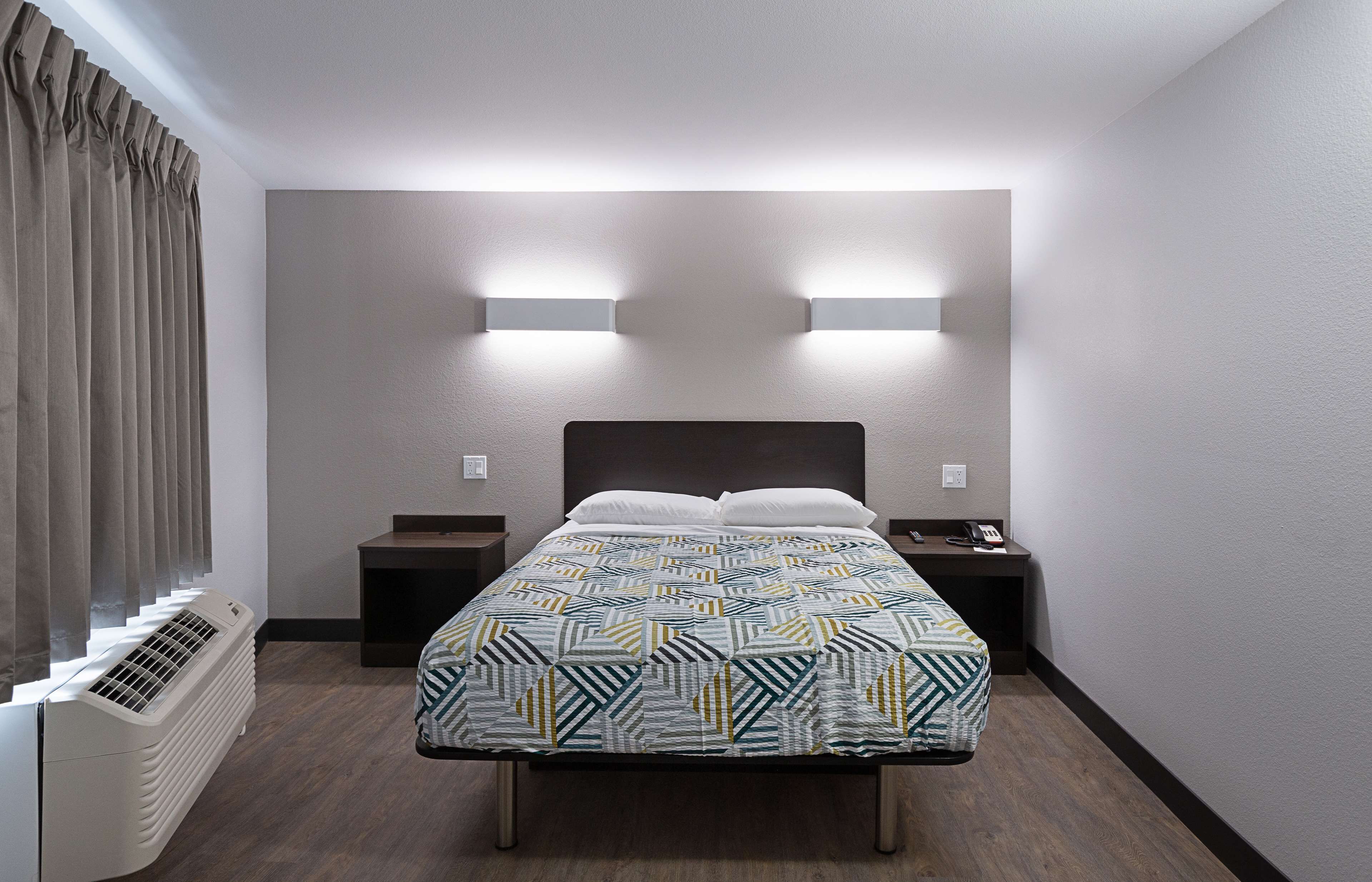 Habitación de hotel con cama, mesitas de noche, calefacción y luces fijadas a la pared.