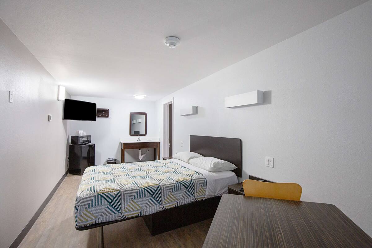 A hotel room with a bed, bedside table, and a desk.