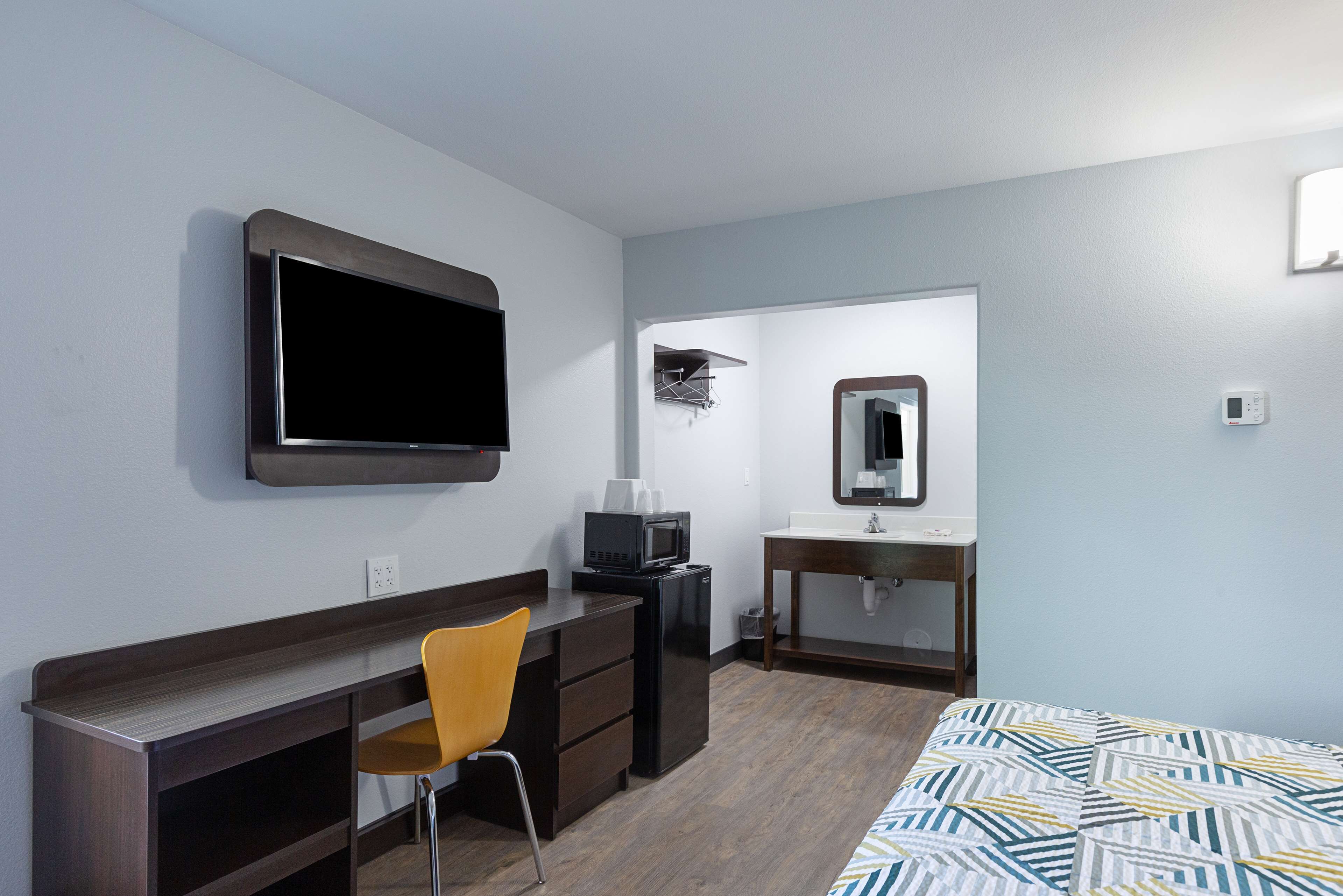 A hotel room with a desk, chair, microwave, and a bed with a patterned bedspread.