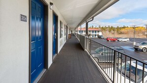 Un couloir avec des portes bleues, un balcon avec une balustrade et une vue sur les voitures garées et les arbres.