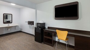 Une chambre d’hôtel équipée d’un téléviseur à écran plat fixé au mur, d’un lavabo avec miroir, d’un petit réfrigérateur et d’un bureau en bois avec une chaise.