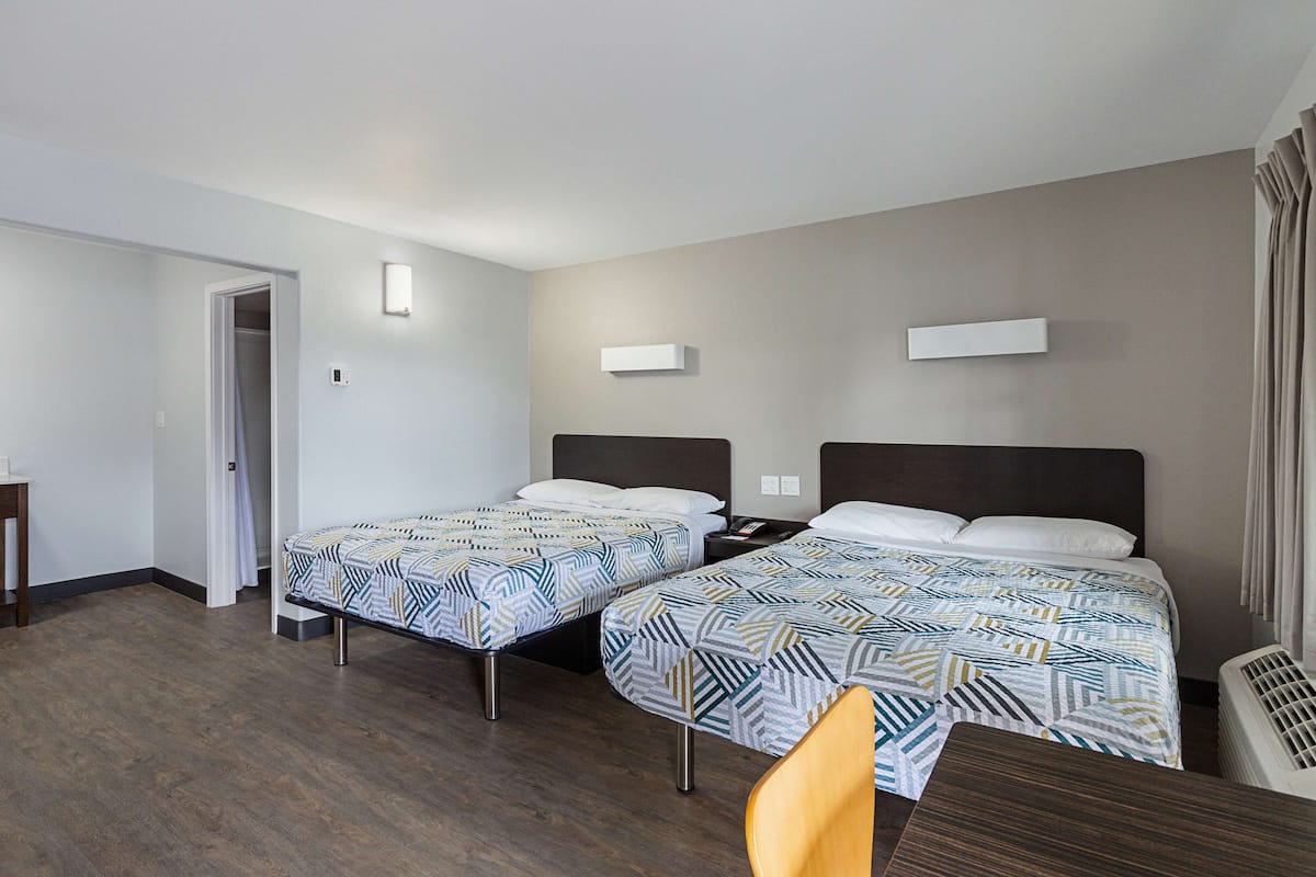 A hotel room with two beds, a desk, and a chair.