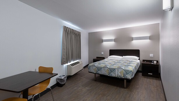 Une chambre d’hôtel comprenant un lit, des tables de chevet, un bureau avec une chaise, une fenêtre avec des rideaux et un luminaire fixé au mur.