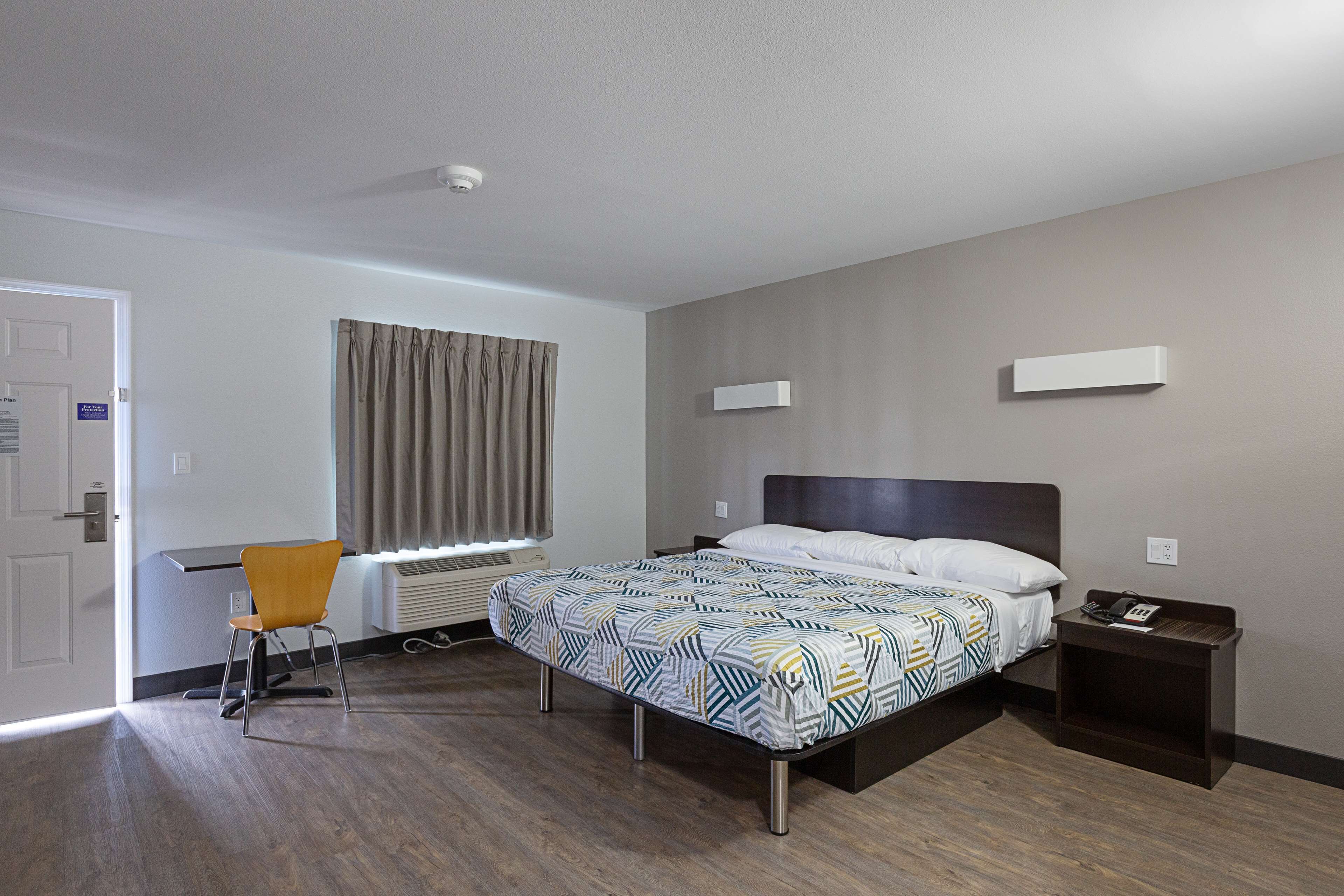 A hotel room with a bed, a desk, a chair, and a window with curtains.