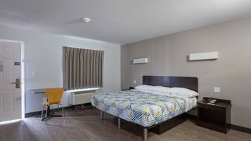 A hotel room with a bed, a desk, a chair, and a window with curtains.