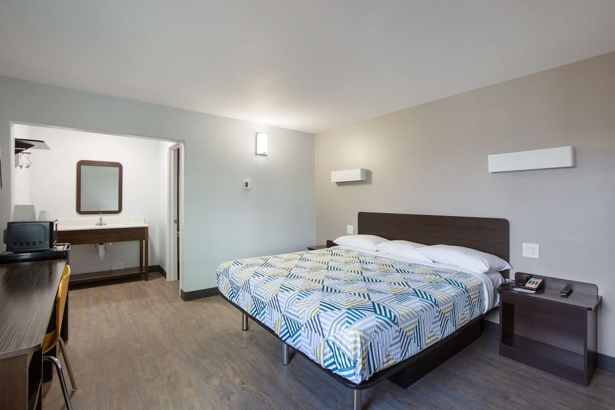 A hotel room with a bed, bedside table, and a desk with a chair.