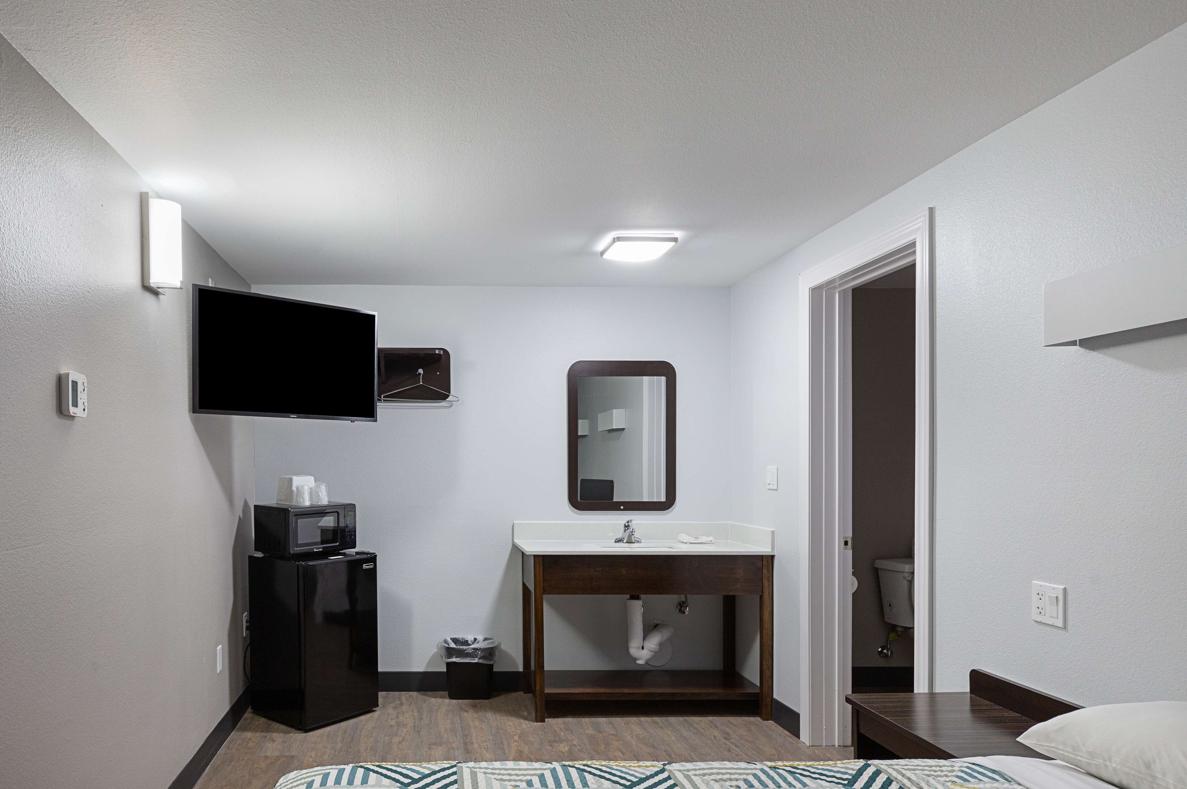 Une chambre d’hôtel équipée d’un téléviseur à écran plat fixé au mur, d’une coiffeuse en bois avec un miroir, d’un lavabo et d’un petit réfrigérateur.