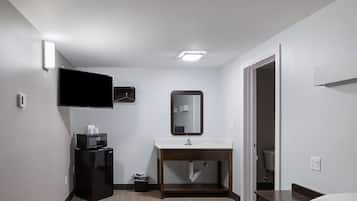 Une chambre d’hôtel équipée d’un téléviseur à écran plat fixé au mur, d’une coiffeuse en bois avec un miroir, d’un lavabo et d’un petit réfrigérateur.