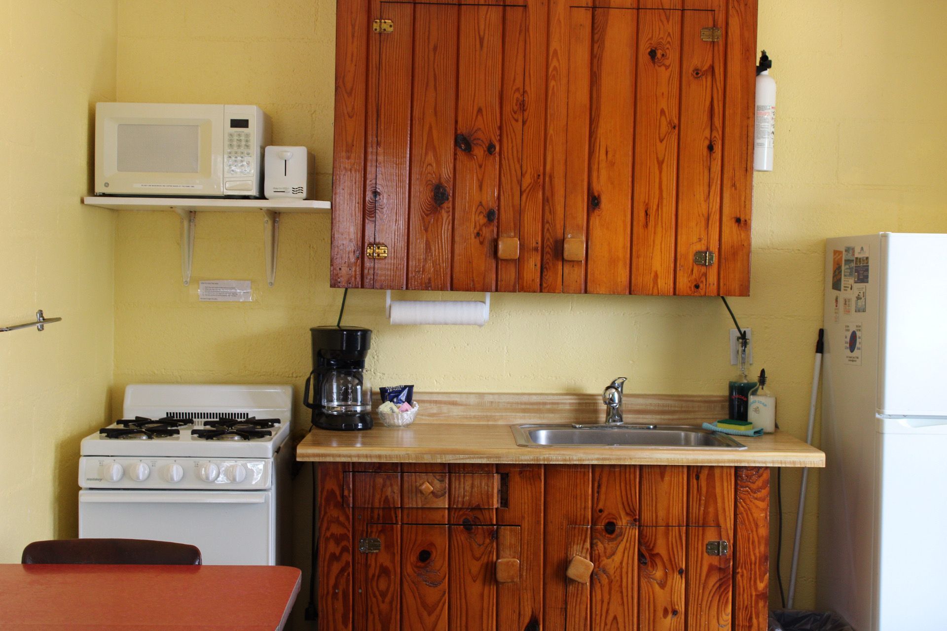 A compact kitchen with wooden cabinets, a microwave, a stove, a sink, and a refrigerator.