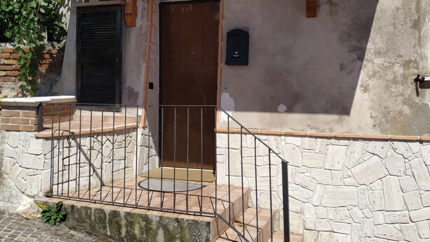 A building with a stone facade, a wooden porch, a metal gate, and a door with a number '13' sign. - Casa Pif: quiet, pretty and welcoming (Frosinone)