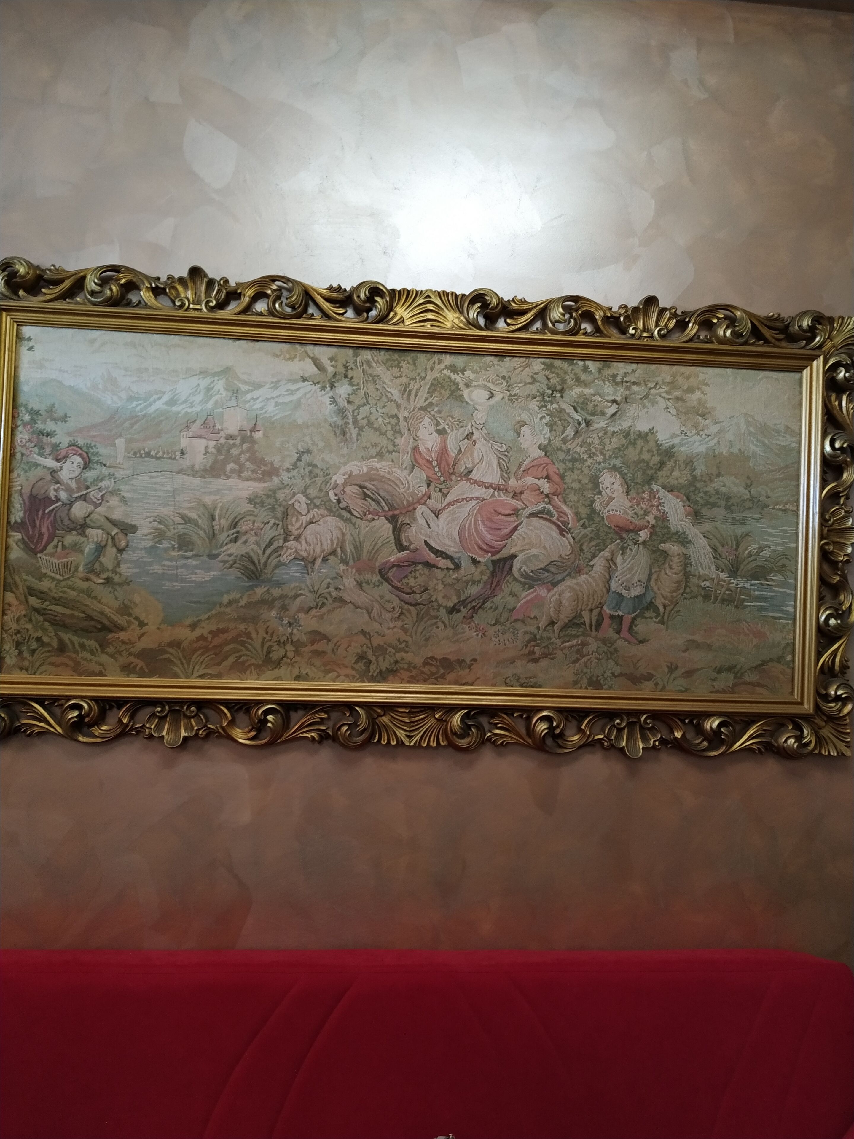 Un tableau encadré, fixé au mur, avec un cadre doré orné, représentant une scène pastorale avec des personnages et des moutons.