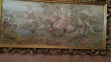 Un tableau encadré, fixé au mur, avec un cadre doré orné, représentant une scène pastorale avec des personnages et des moutons.