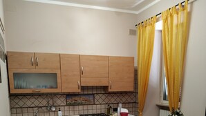 A compact kitchen with wooden cabinets, a gas stove, and a sink. There's a small dining table with chairs. Yellow curtains are on the window. - Casa Pif: quiet, pretty and welcoming (Frosinone)