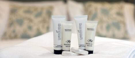 Four tubes of Caroline Henry hair and body wash on a bed with pillows.
