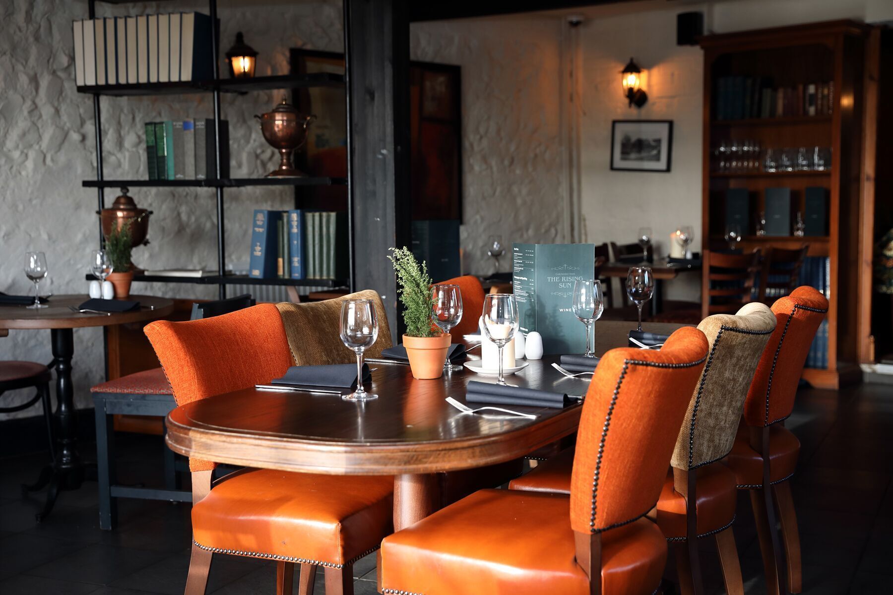A dining area with a round table, orange upholstered chairs, and a menu titled "The Rising Sun."