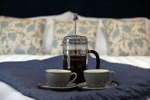 A French press coffee maker with two cups on a bed.