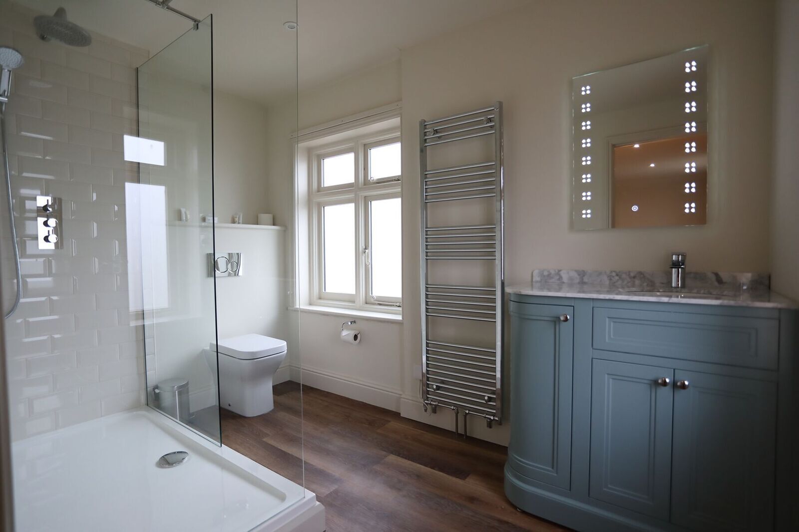 Un baño con cabina de ducha de vidrio, inodoro, ventana, toallero y tocador con espejo.