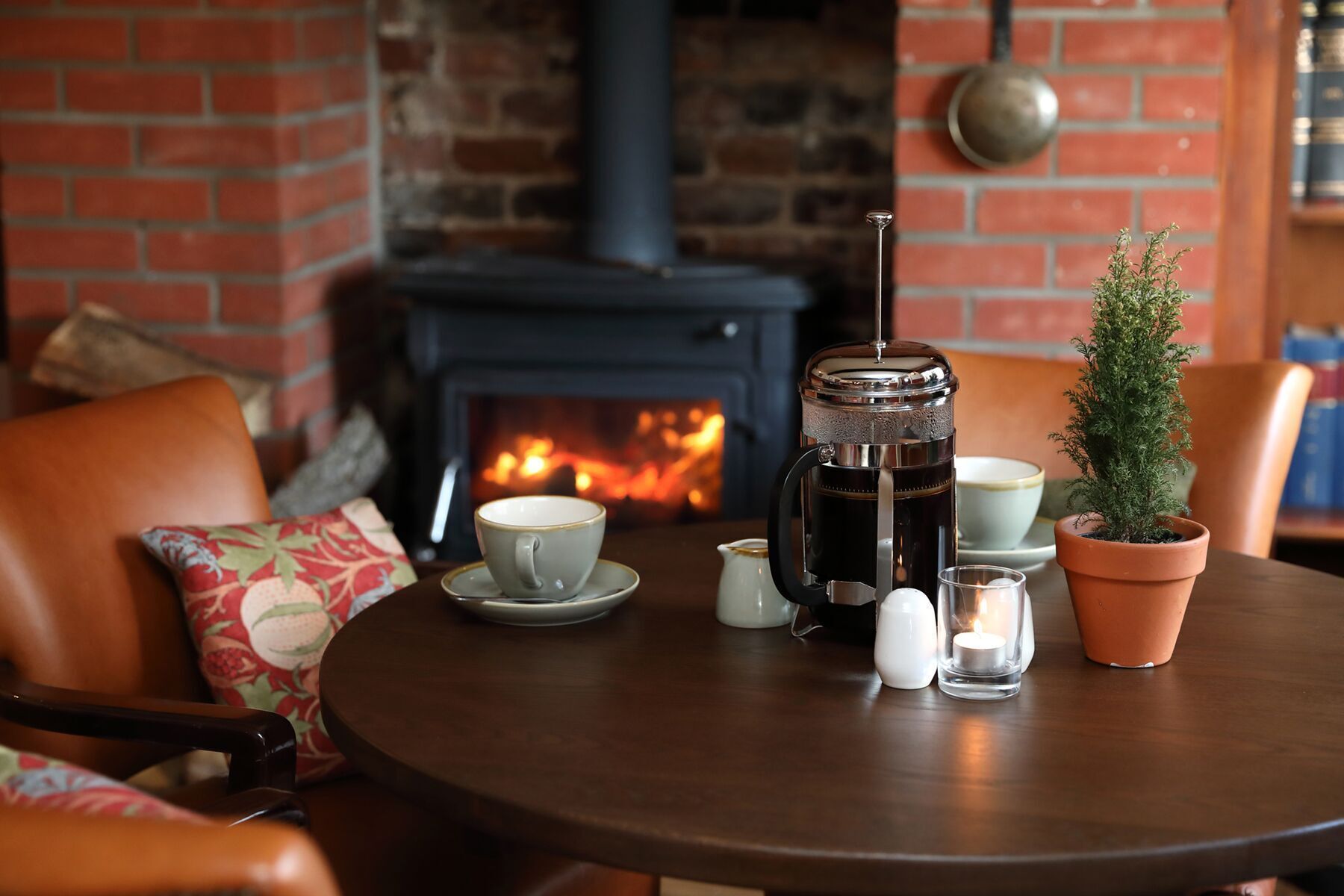 A cozy seating area with a table set for a meal, a fireplace, and a small potted plant.