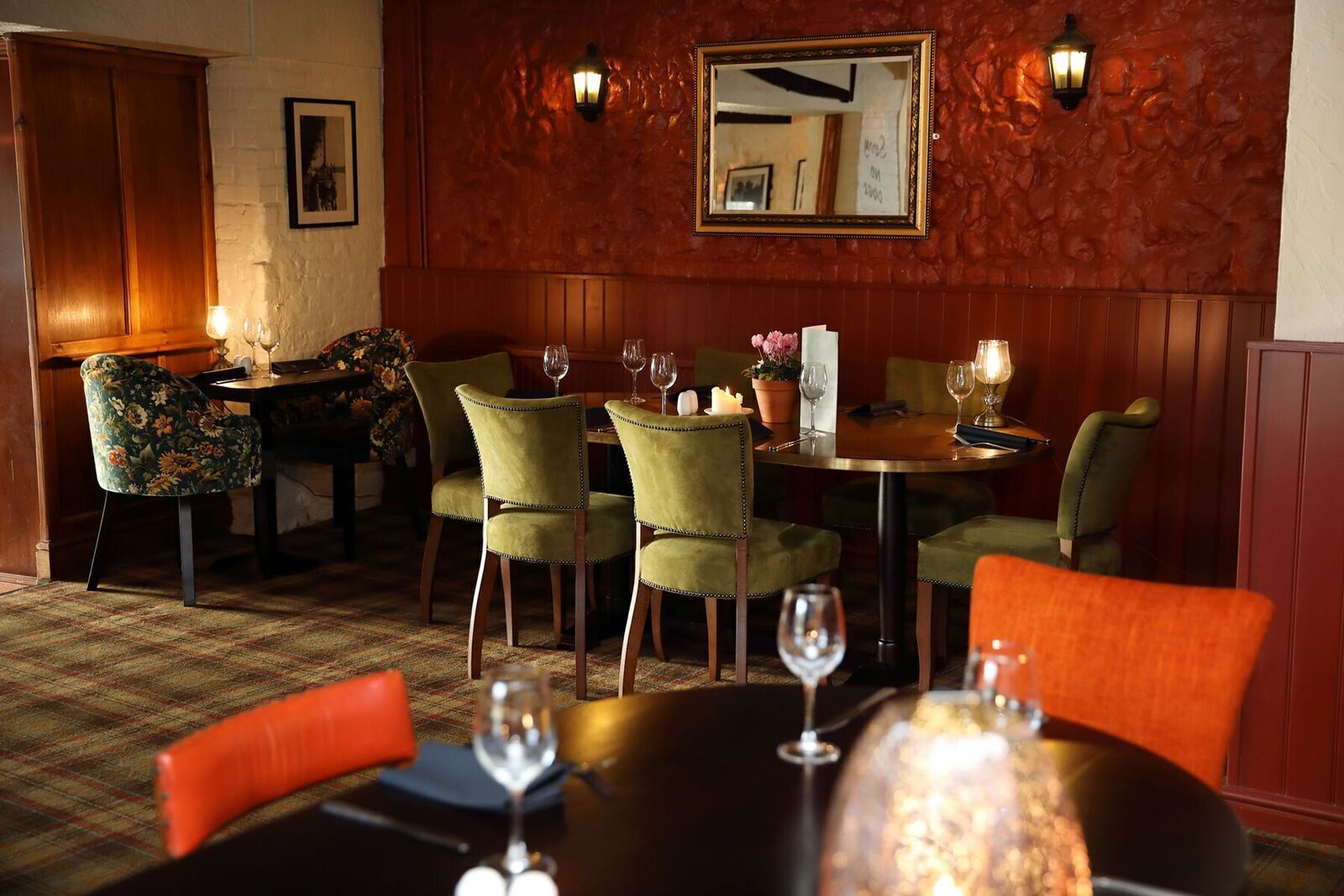 A dining area with green upholstered chairs, a round table, and candlelit ambiance.