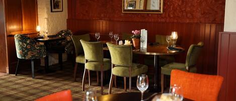 A dining area with green upholstered chairs, a round table, and candlelit ambiance.