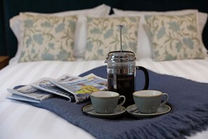 A bed with a French press coffee maker, two cups, and a magazine on a blue blanket.