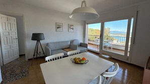 A modern living room with a white sofa, a dining table with fruit, a floor lamp, and a balcony with a view. - Agi Horitzo 11 Apartamento for rent in Roses Girona. (Roses)