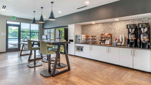 A modern kitchen area with a bar counter, seating, and coffee machines. - Extended Stay America Suites Colonial Heights Fort Lee (Colonial Heights)
