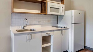 A compact kitchen with white cabinets, a stainless steel sink, a microwave, and a refrigerator. - Extended Stay America Suites Colonial Heights Fort Lee (Colonial Heights)