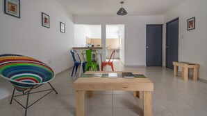 Ein modernes Wohnzimmer mit Couchtisch aus Holz, bunten Stühlen und Blick in die Küche.
