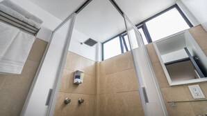 Ein modernes Badezimmer mit Duschabtrennung aus Glas, beigen Fliesen, einem Handtuchhalter, einem Spiegel und einem Fenster für natürliches Licht.