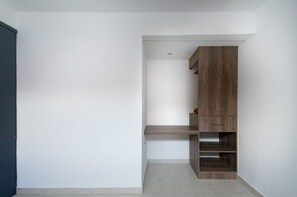 A minimalist room with a built-in wooden shelving unit against a white wall, a grey floor, and a dark door.