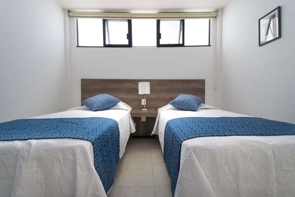A room with two beds, a nightstand, a lamp, and a window.